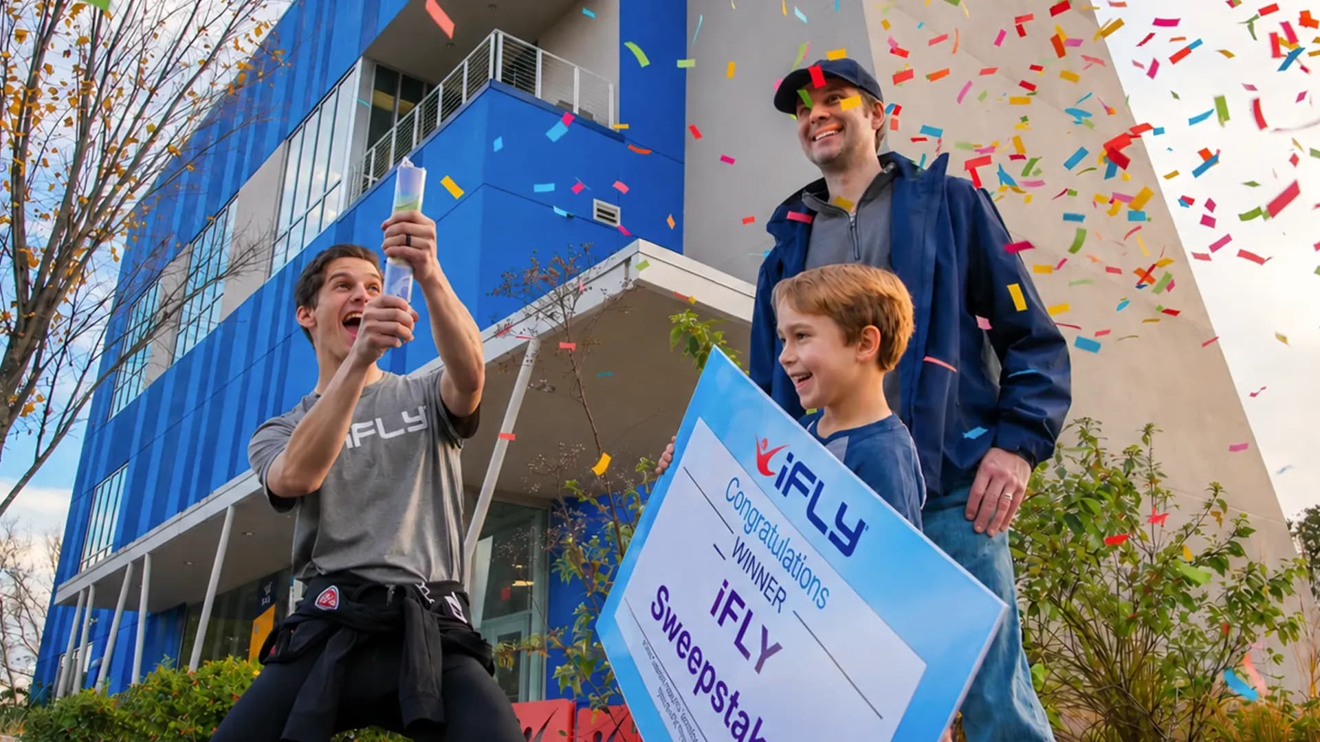 Man takes selfie with father and child holding "iFLY Sweepstakes Winner" sign.