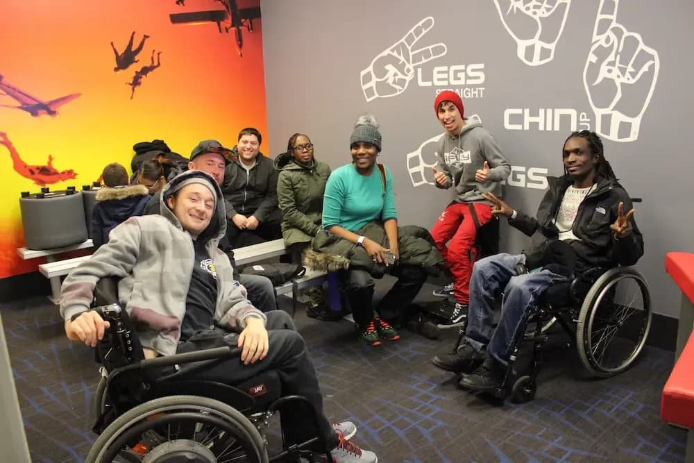 A diverse group of smiling people, some in wheelchairs, gathered in a colorful room.