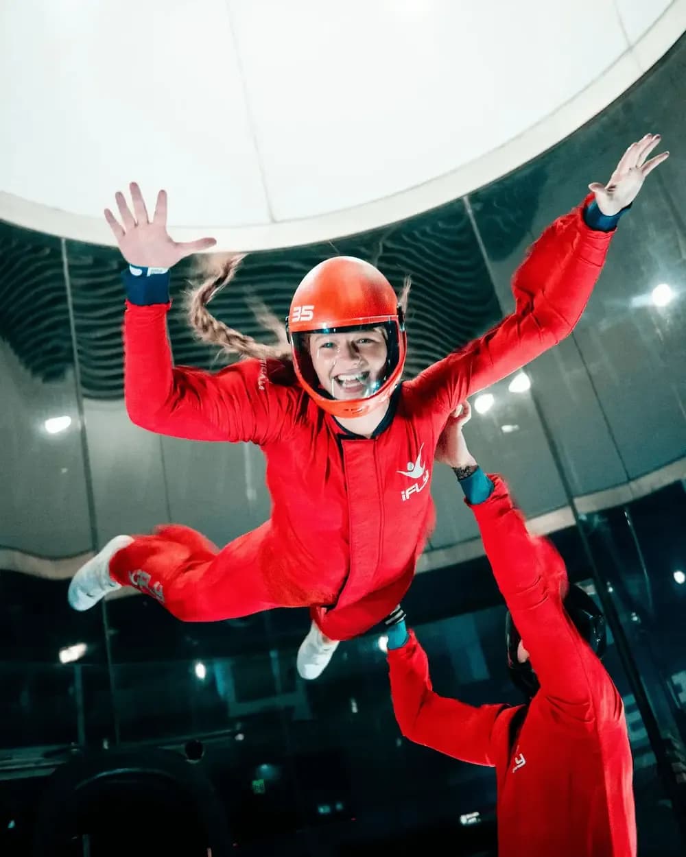 Happy woman in red jumpsuit indoor skydiving, assisted by an instructor.