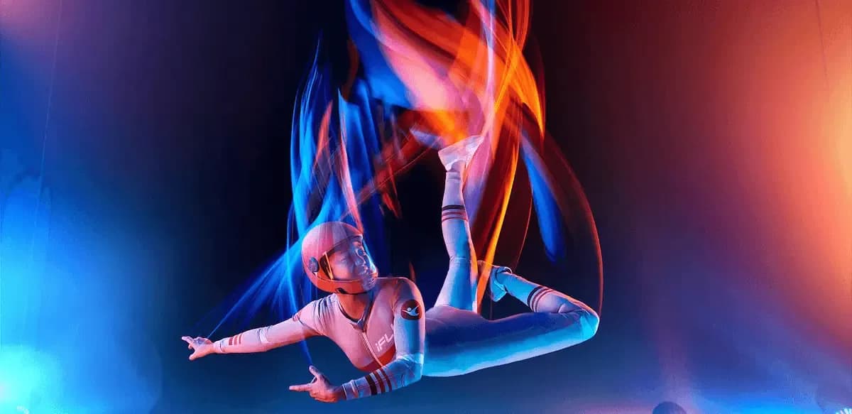 Performer in a futuristic suit suspended, surrounded by dynamic blue and orange light trails.