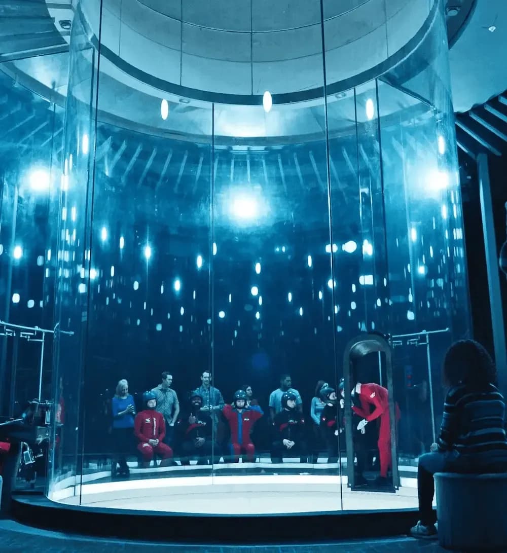 Person in red suit floating inside a blue-lit indoor skydiving wind tunnel.