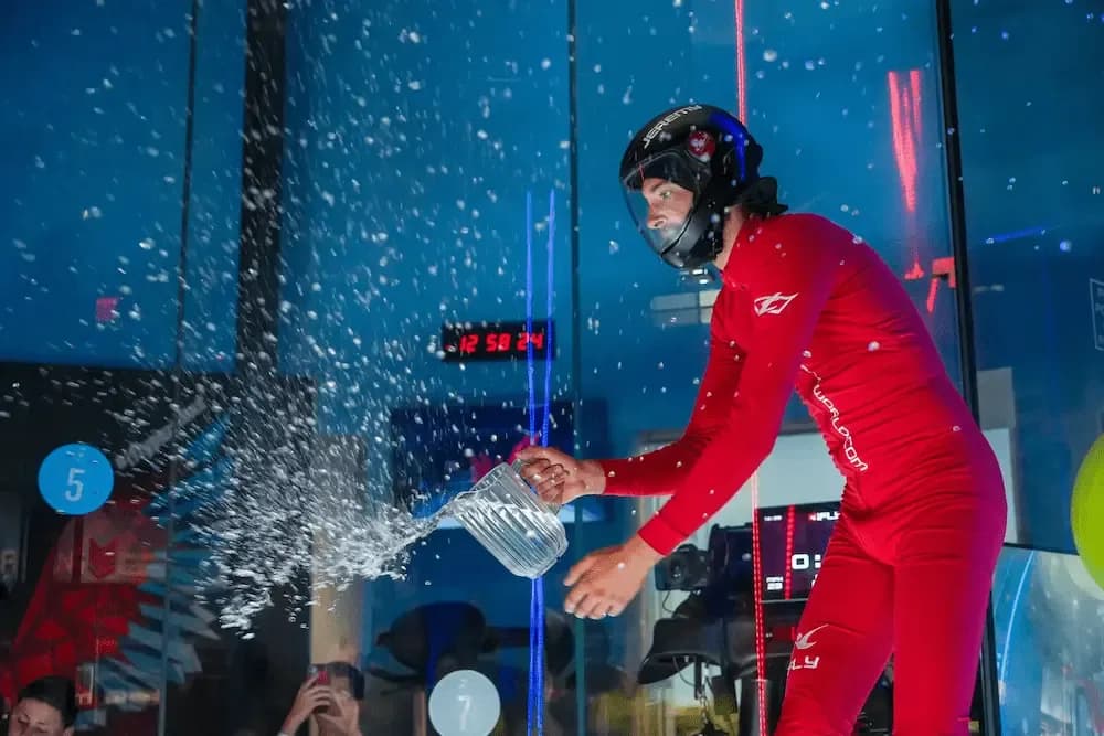 Person in red suit and helmet pours water, creating a dramatic splash in a blue-lit tunnel.