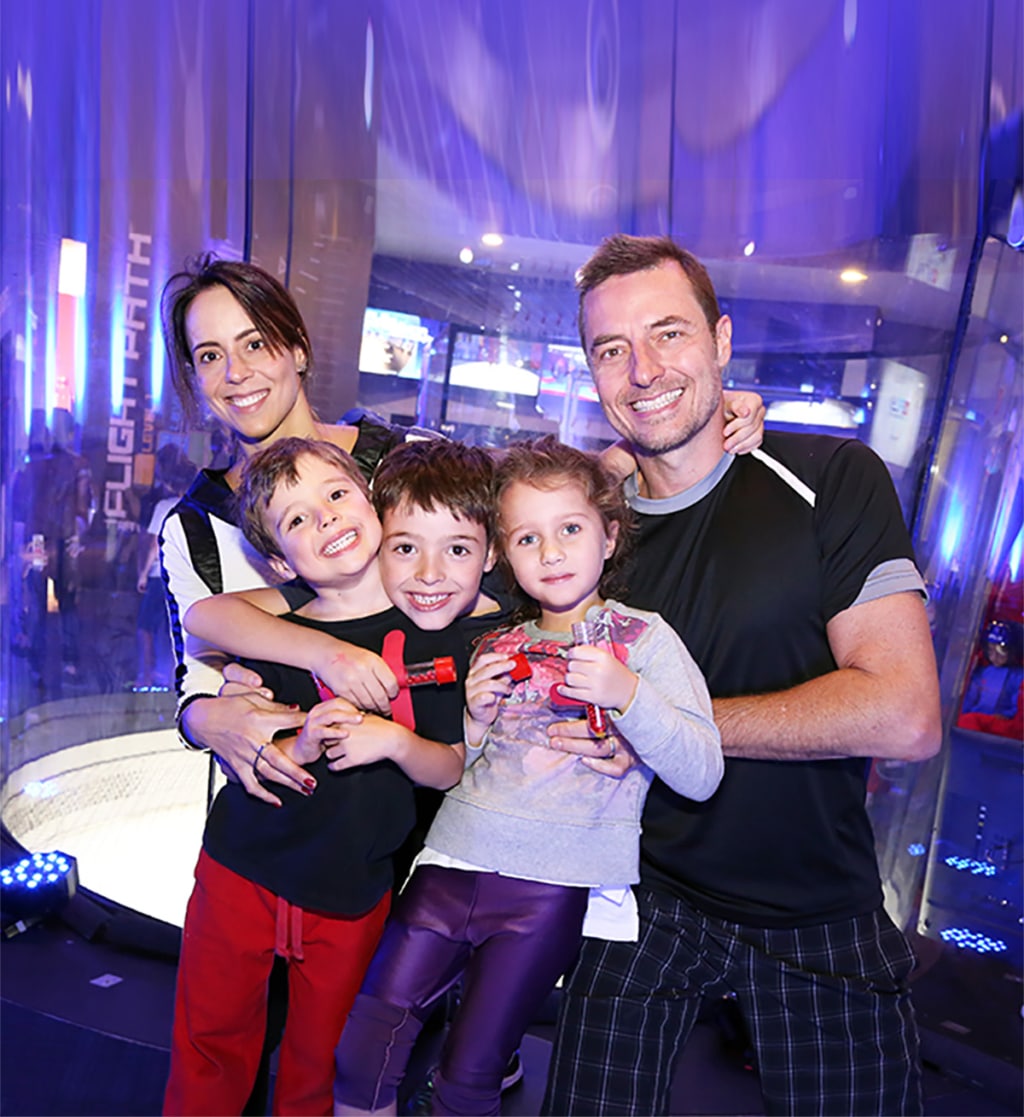 Parents with three children smiling and posing in front of an indoor skydiving tunnel