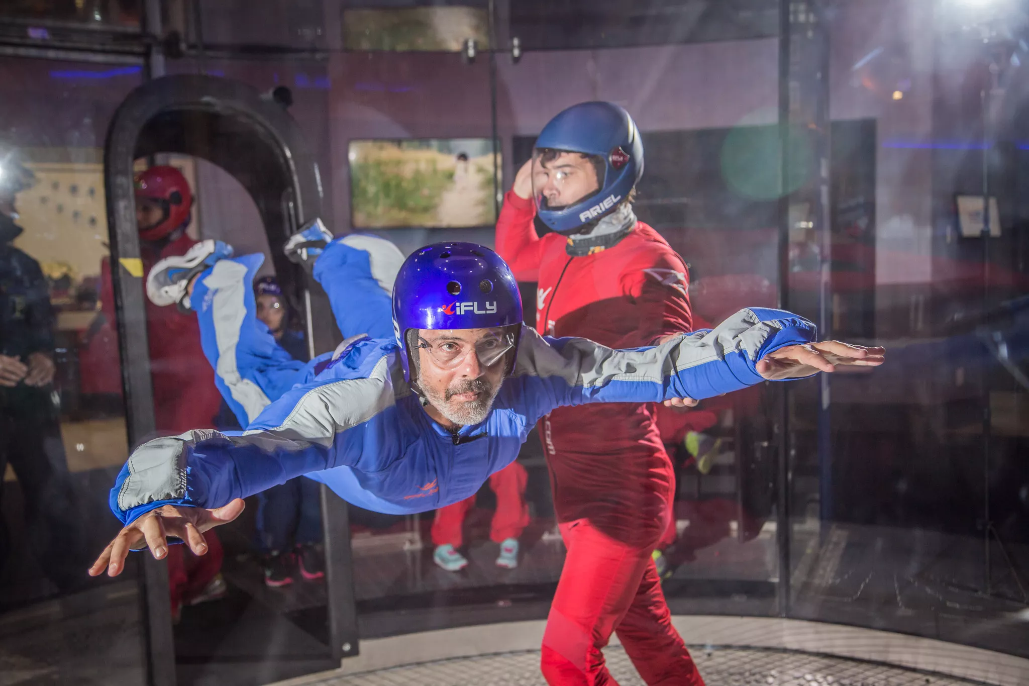 Older man flying in an indoor skydiving tunnel with an iFLY instructor alongside him