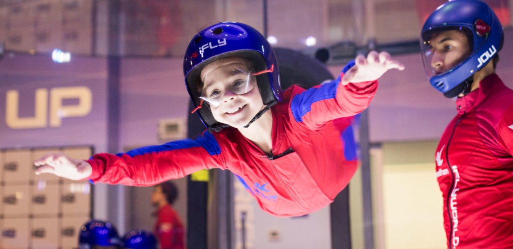 Young child flying in the tunnel with his instructor helping alongside him